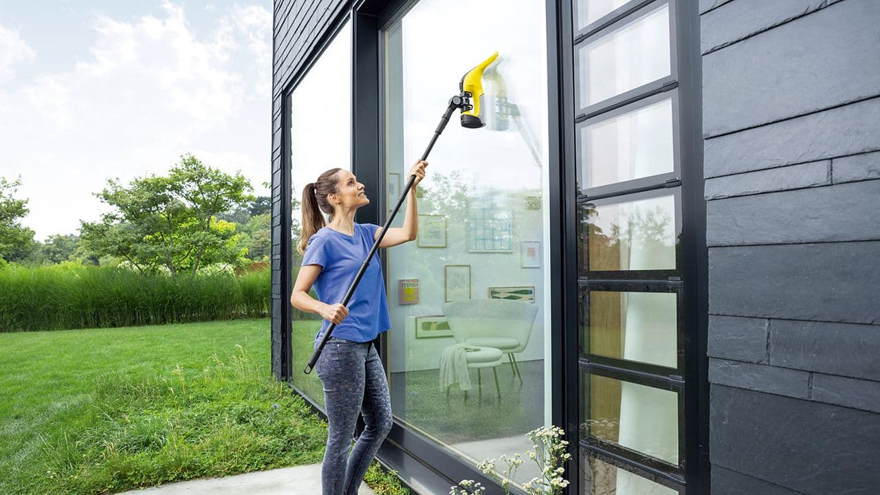 Kvinne som viser hvordan vaske vinduer ute med vindusvasker og forlengerskaft.