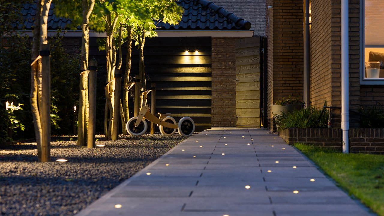 Inngangsparti som er opplyst med utendørsbelysning på vegg og innfelt i steinheller.