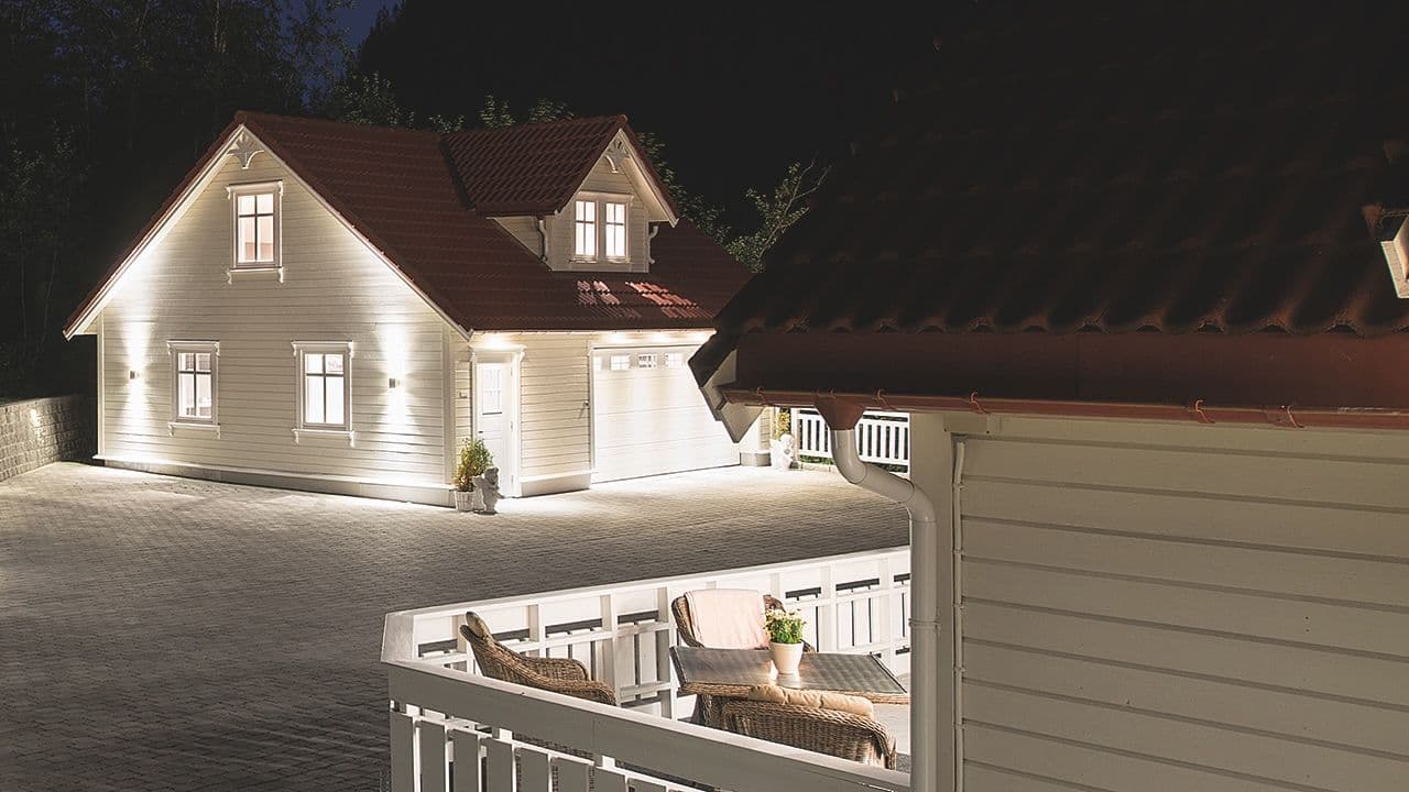 Hvitt hus med garasje som er opplyst med utebelysning til garasje.