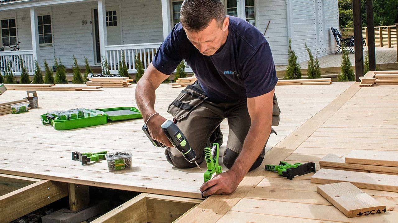 Mann som skrur skruer på terrasse.