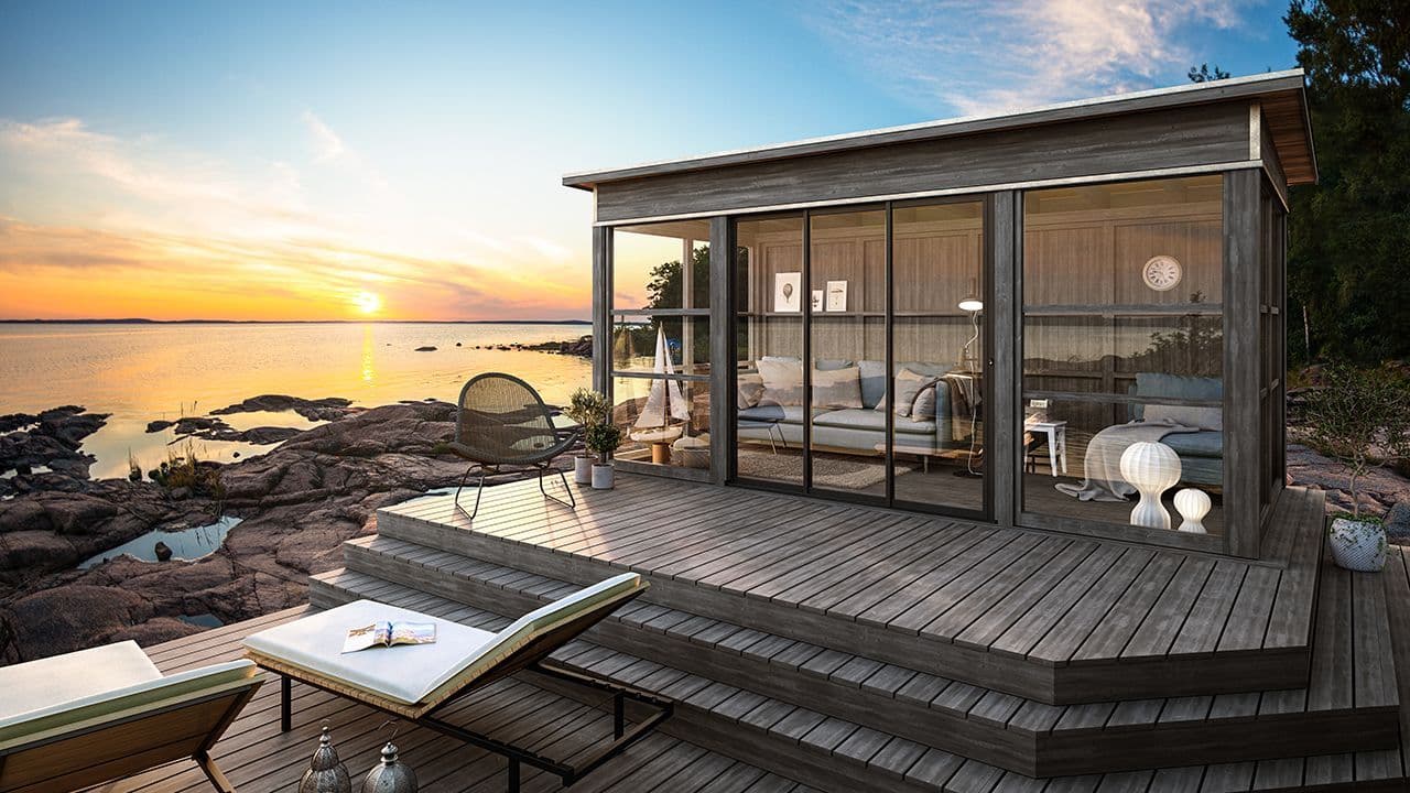 Hagestue med store glassflater ved sjøen.