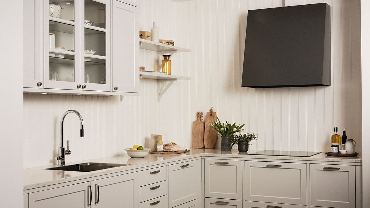 Beige, landlig kjøkken med åpne hyller, vitrinefronter på overskaper og svart kjøkkenhette.