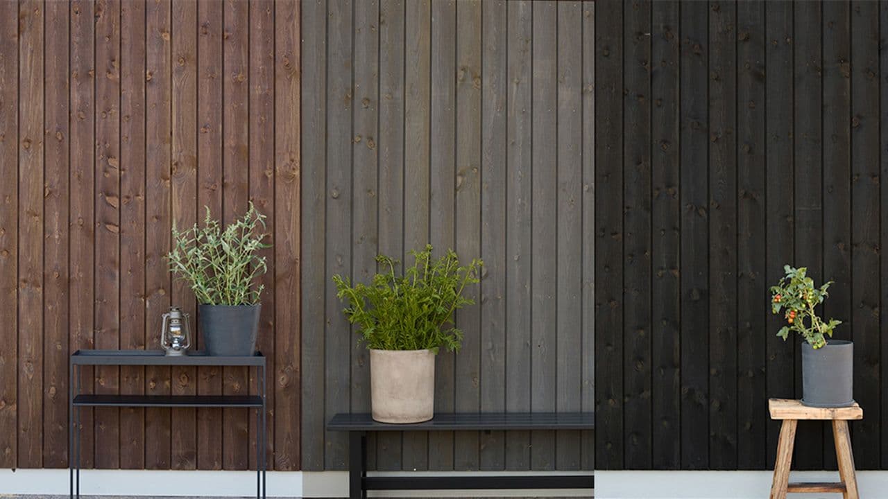 Tre husvegger med kledning malt i brunt, grått og sort.