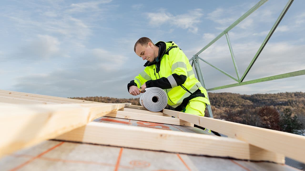 Håndverker i arbeidstøy med refleks som rehabiliterer tak.