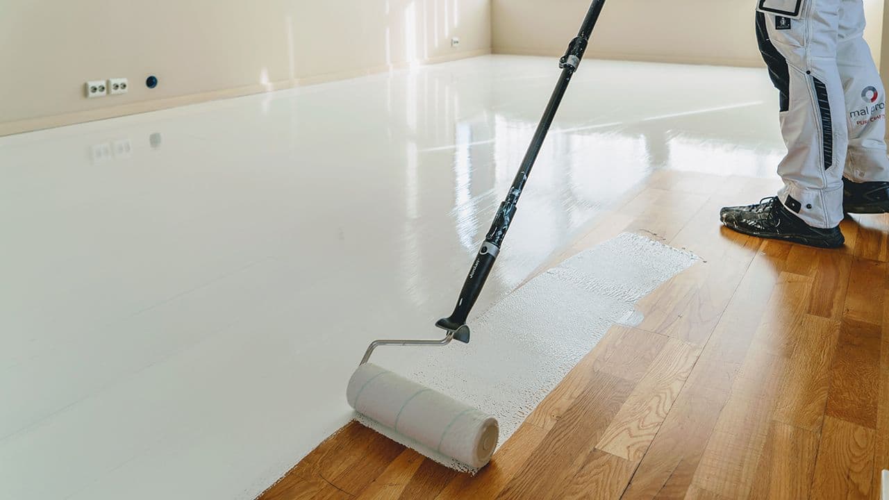 Person som maler gulvet med rulle og gulvmaling.