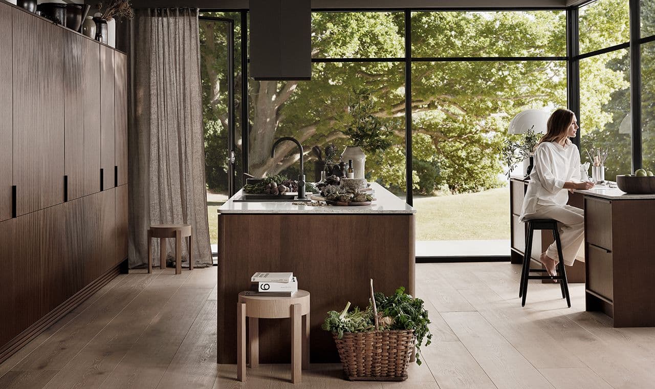 Kvinne som sitter ved skrivebord i rom med åpen kjøkkenløsning.