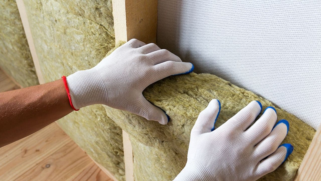 Hender med hansker som setter på plass ROCKWOOL steinullisolasjon i innvendig vegg.