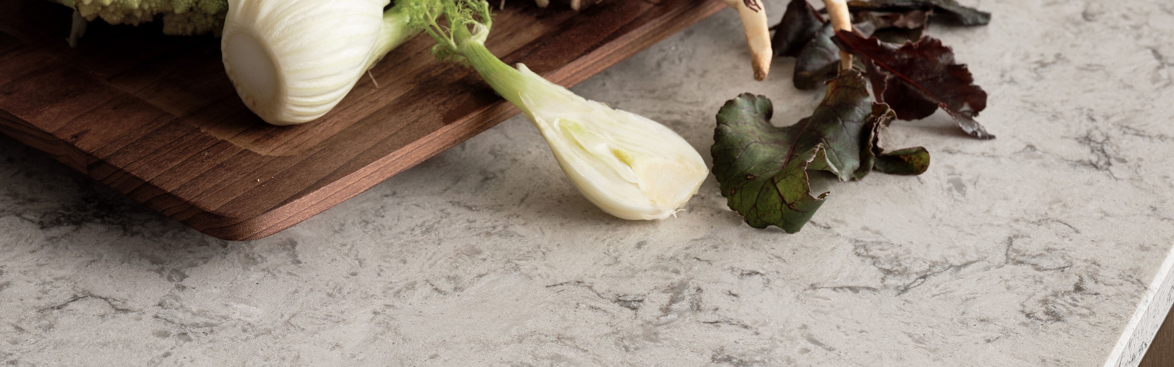 Benkeplate i stein med skjærebrett i tre med grønnsaker på.