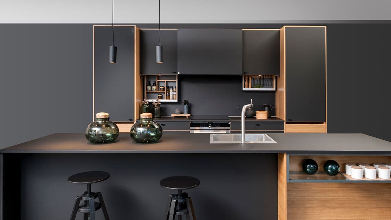 Kjøkkenhette mellom to overskap på sort kjøkken.