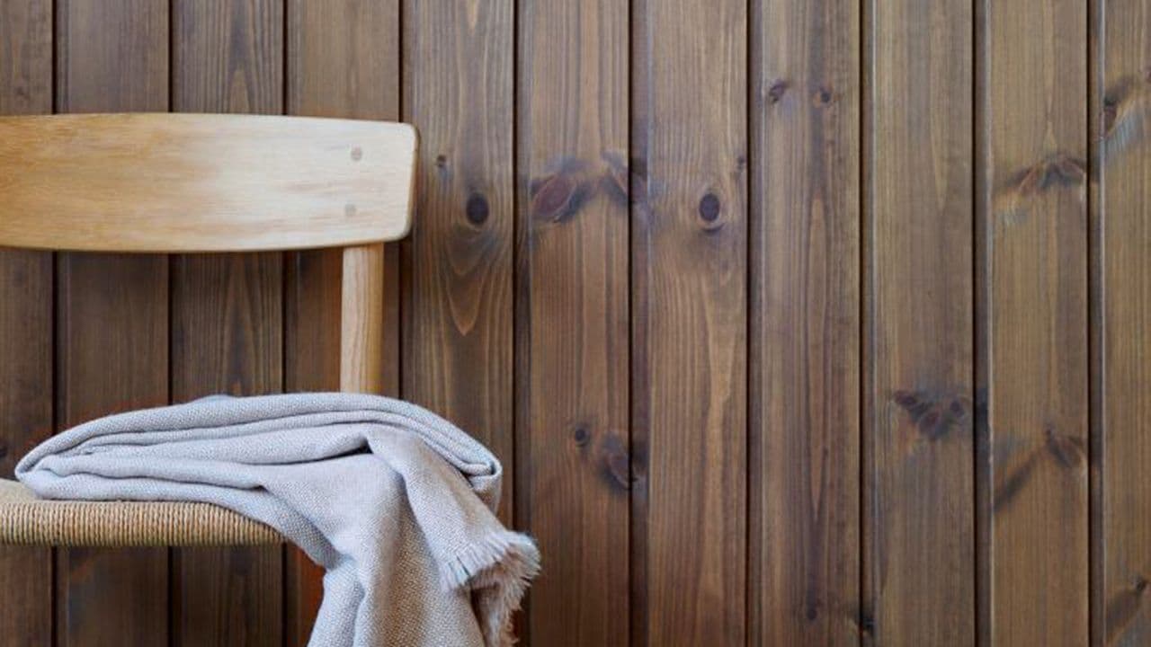 Lys eikestol med pledd på foran veggpanel med brun panellakk fra Jotun i fargen 90024 Dyp Brun.