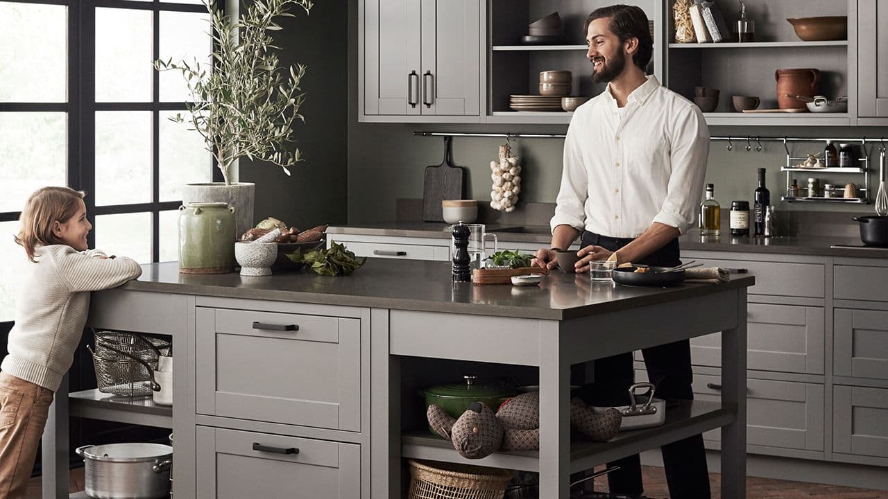 Far og sønn på et landlig kjøkken med kjøkkenøy med åpne hyller i hver ende.