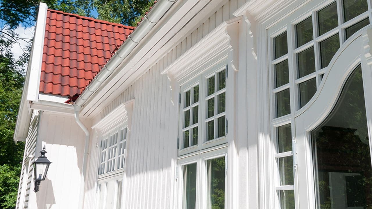 Hvitmalt moderne kledning på gammelt hus med vinduer med sprosser.
