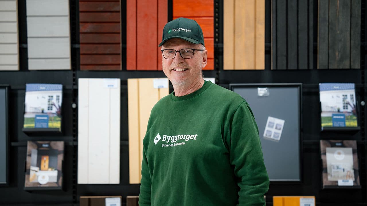 Byggtorget-ansatt i byggevarehus foran en vegg med kledning.