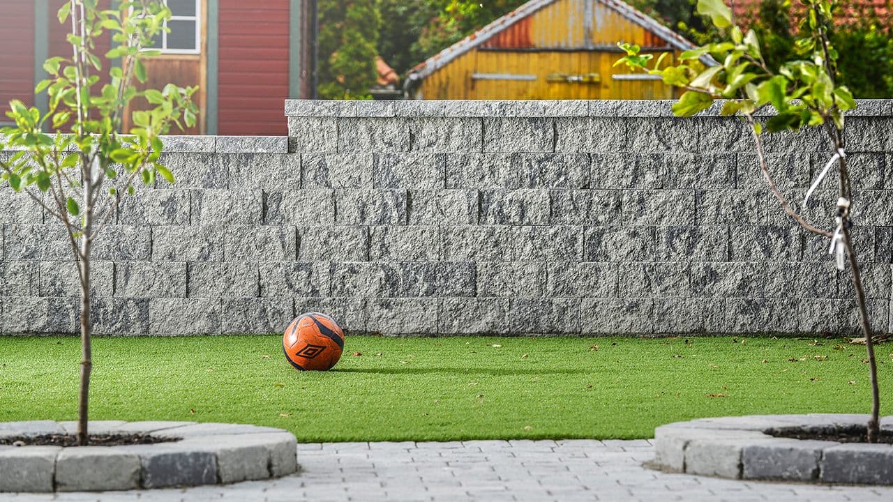 Steinmur med strukturert overflate som støttemur ved gressplen.