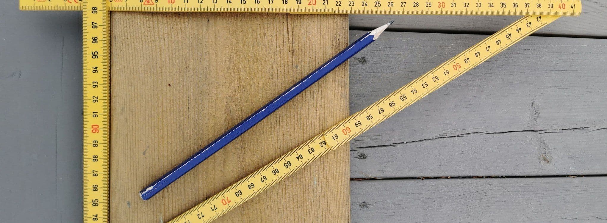 Nærbilde av en utbrettet tommestokk med blyant og planke.