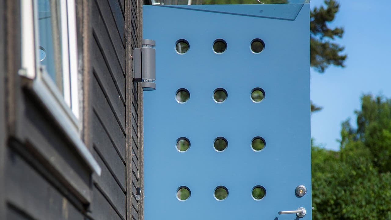 Nærbilde av svart hus med blå ytterdør med mange små glassfelt som er formet som sirkler.