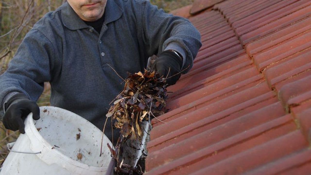 Person som renser takrenne for skitt, løv og mose.