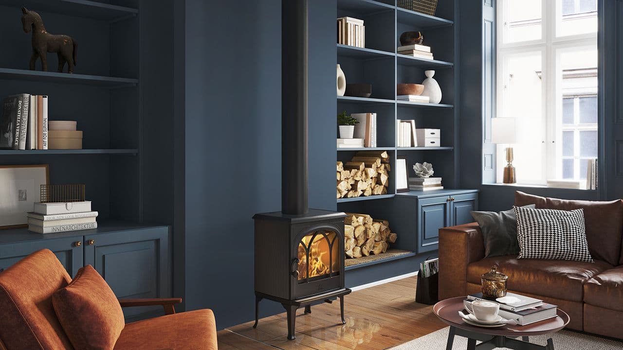 Støpejernsovn F 200 fra Jøtul i blå stue med skinnsofa og brune stoler.