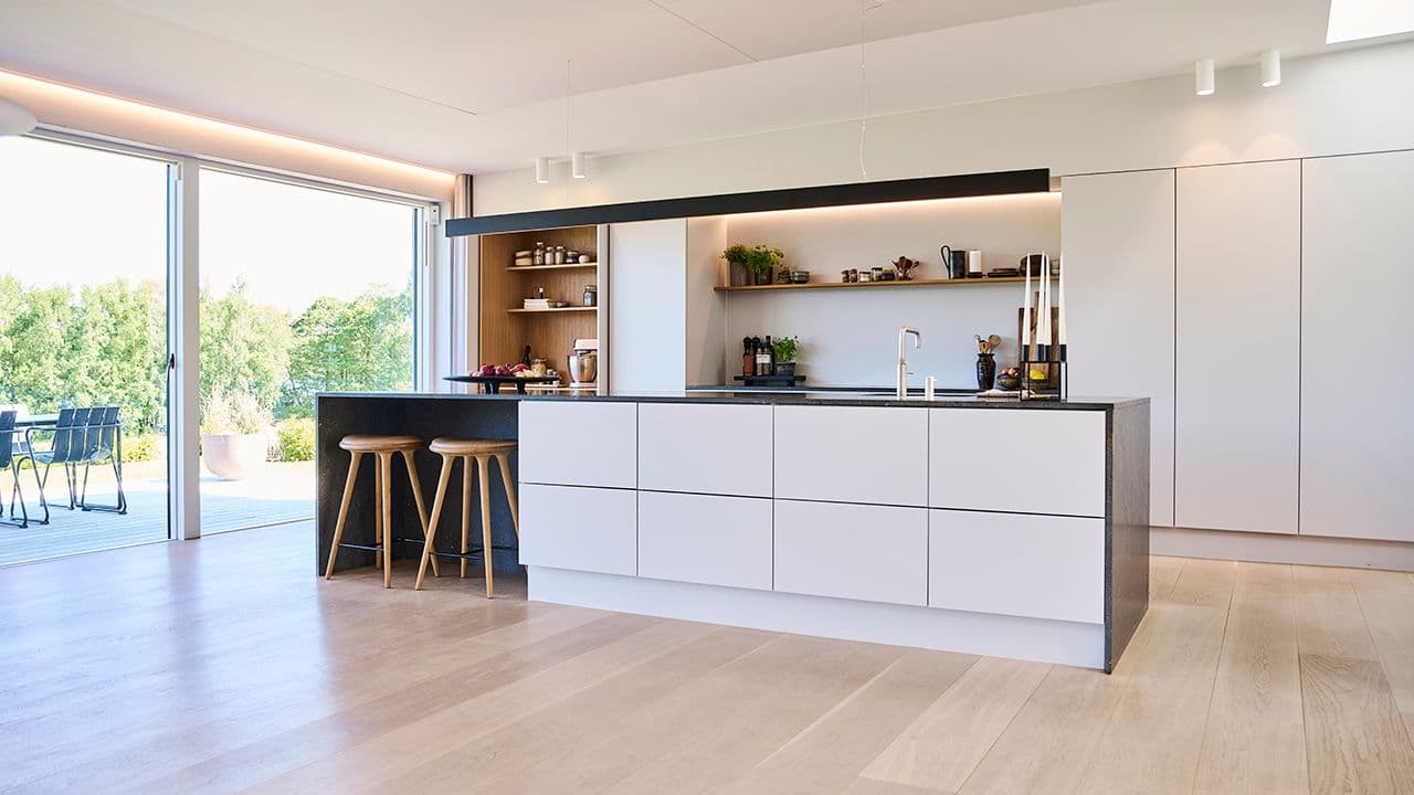 Åpen kjøkkenløsning i hvitt med kjøkkenøy og utgang til terrasse.